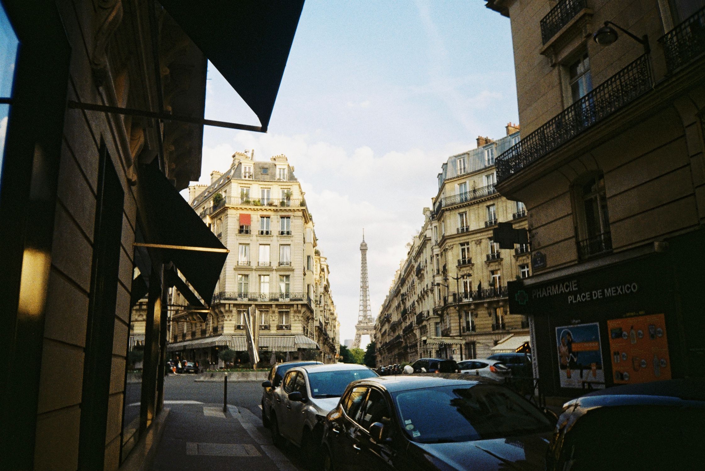 A classic Paris cityscape featuring the Eiffel Tower framed by elegant Haussmann buildings in a busy street