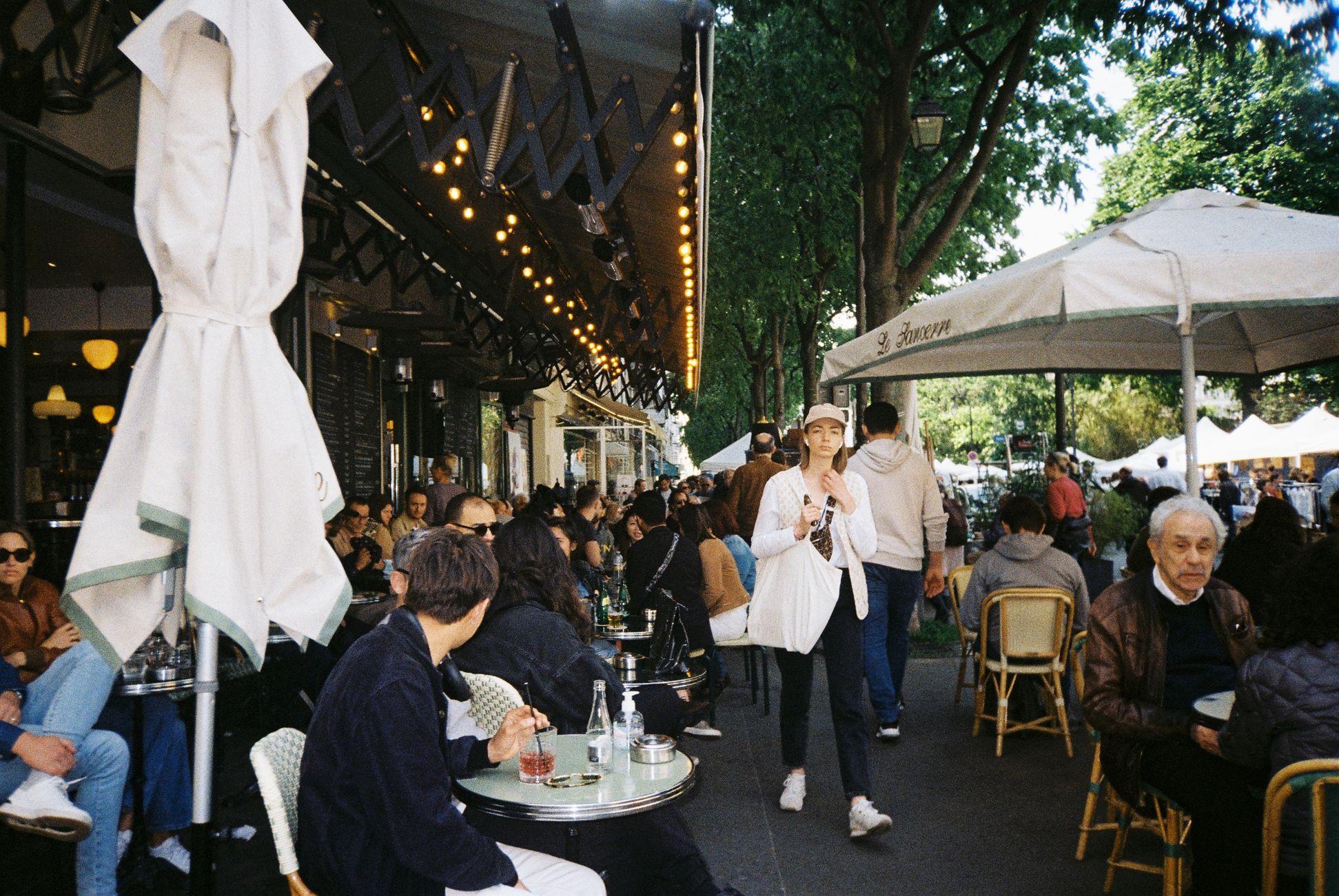 Cozy outdoor city café bustling with people enjoying leisure time under umbrellas and trees.
