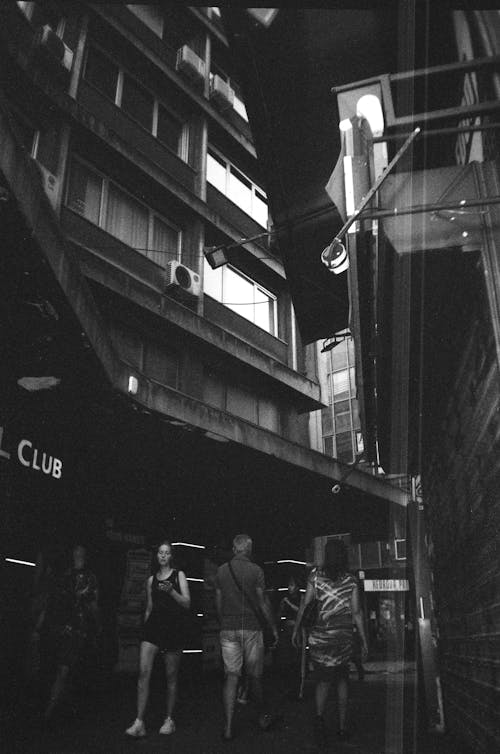 Black and White Picture of People Walking in the Alley between Buildings 