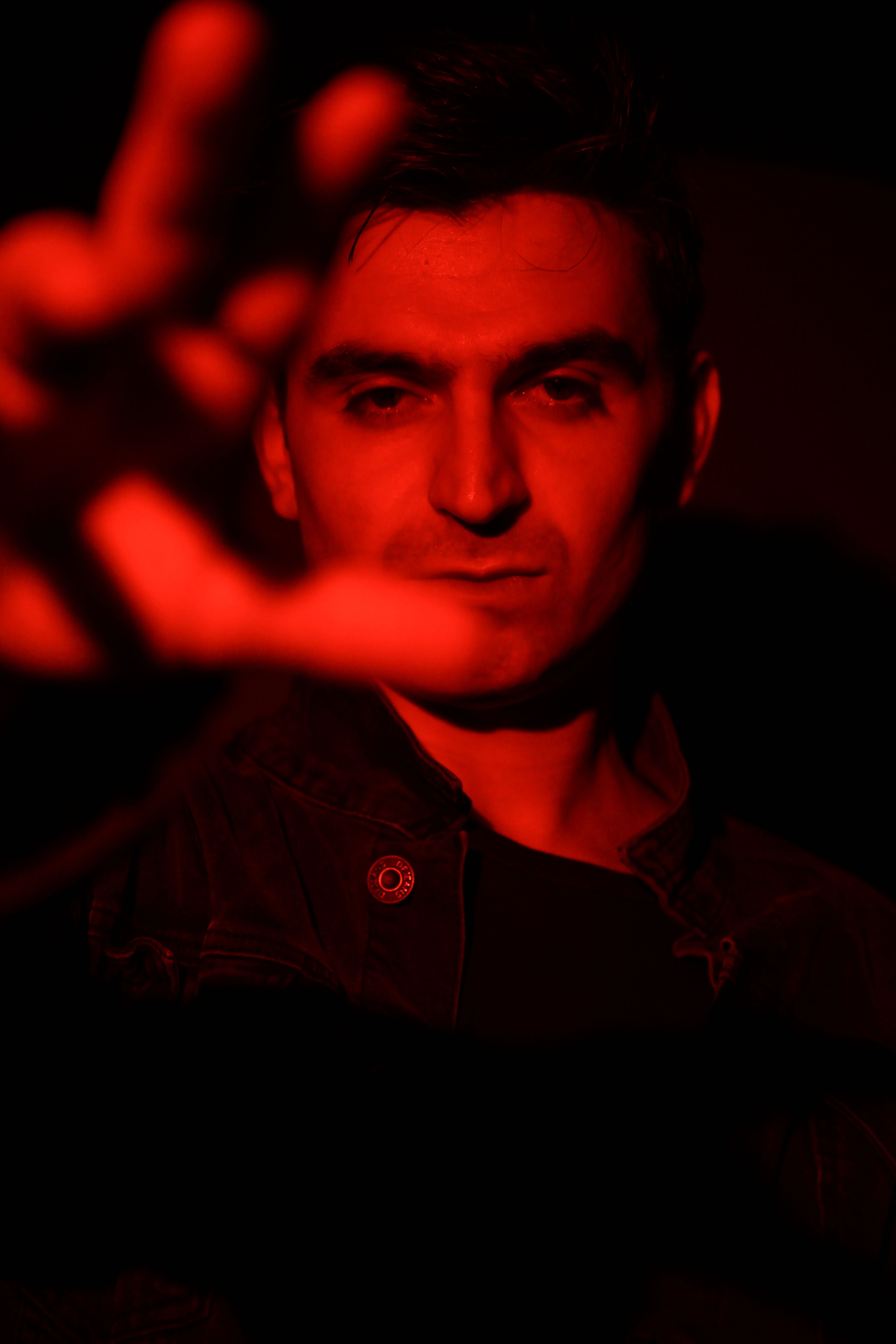 Dramatic portrait of a man under intense red lighting creating a mysterious atmosphere.