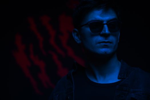 A fashionable man in sunglasses, illuminated by neon blue light, exudes a mysterious vibe.