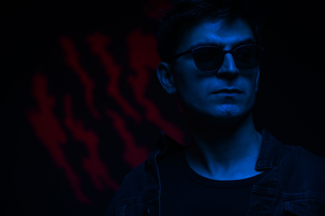a fashionable man in sunglasses illuminated by neon blue light exudes