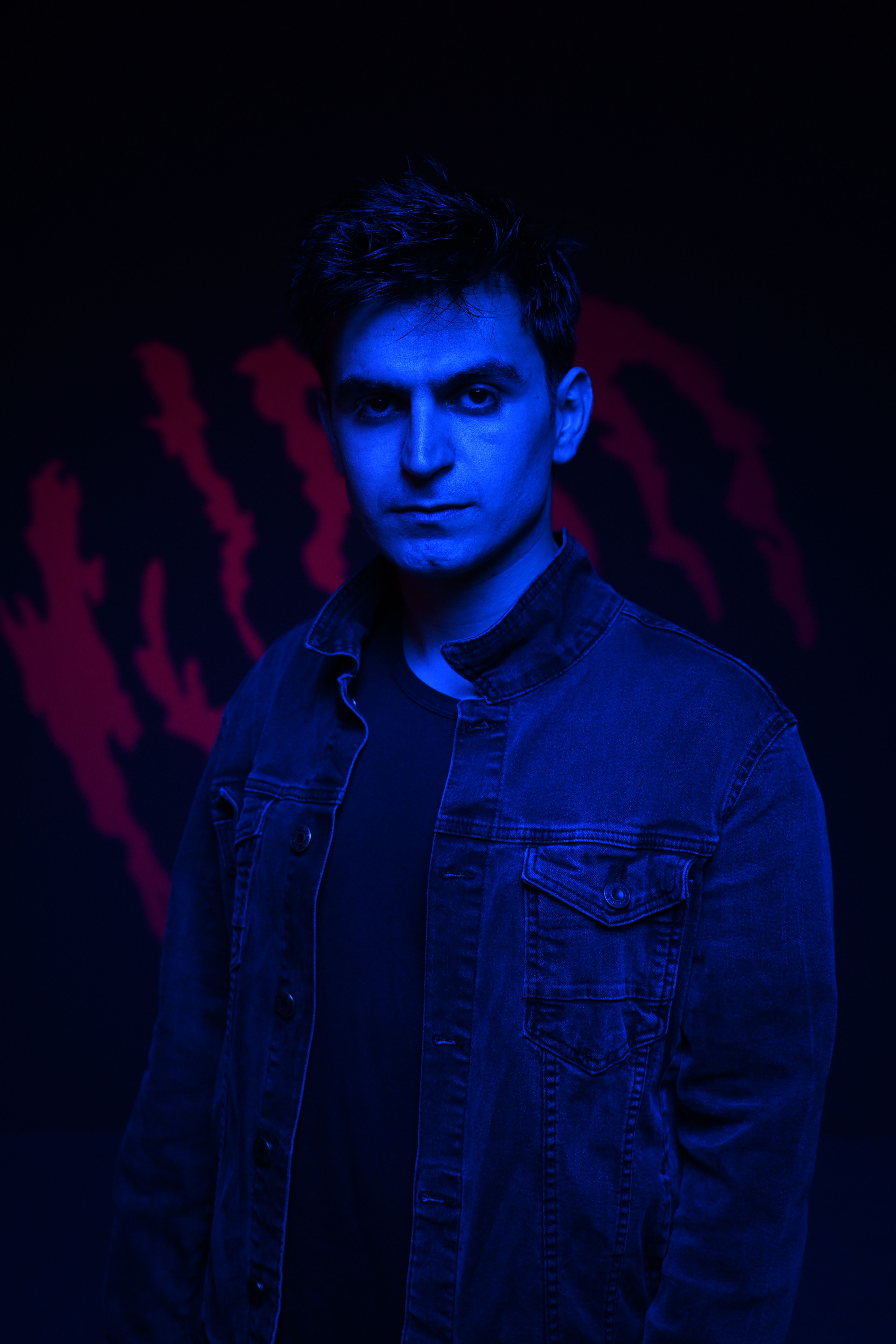 Stylish portrait of a man wearing a jean jacket under dramatic blue lighting.