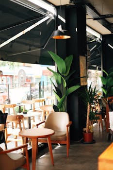 Charming cafe interior with wooden chairs, potted plants, and natural light creating a cozy atmosphere.