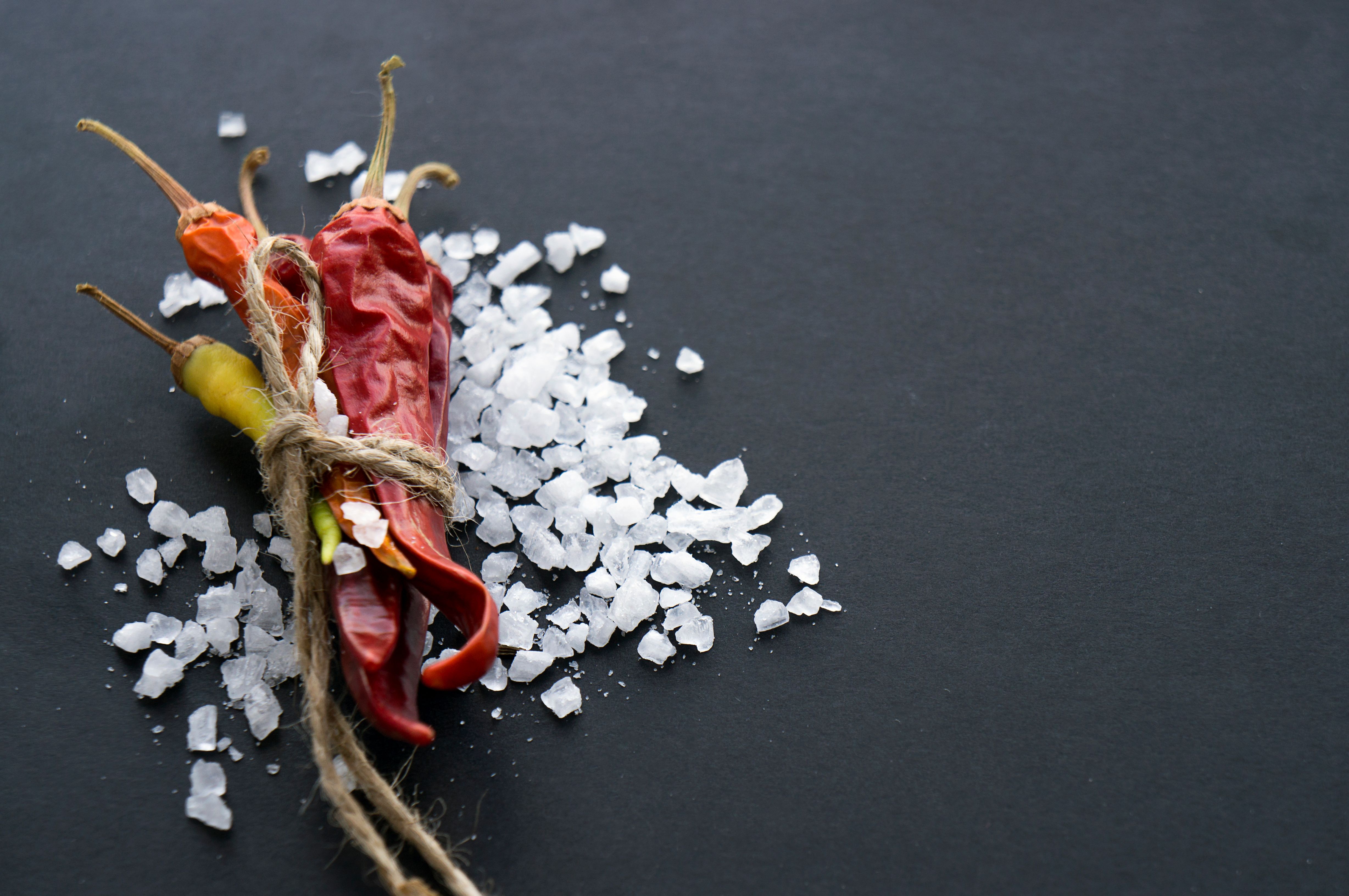A close-up view of vibrant peppers bound by string, surrounded by coarse salt on a gray background.