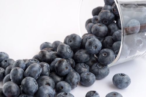 Free A close-up view of fresh blueberries spilling from a glass cup on a white background, showcasing vibrant colors and textures. Stock Photo