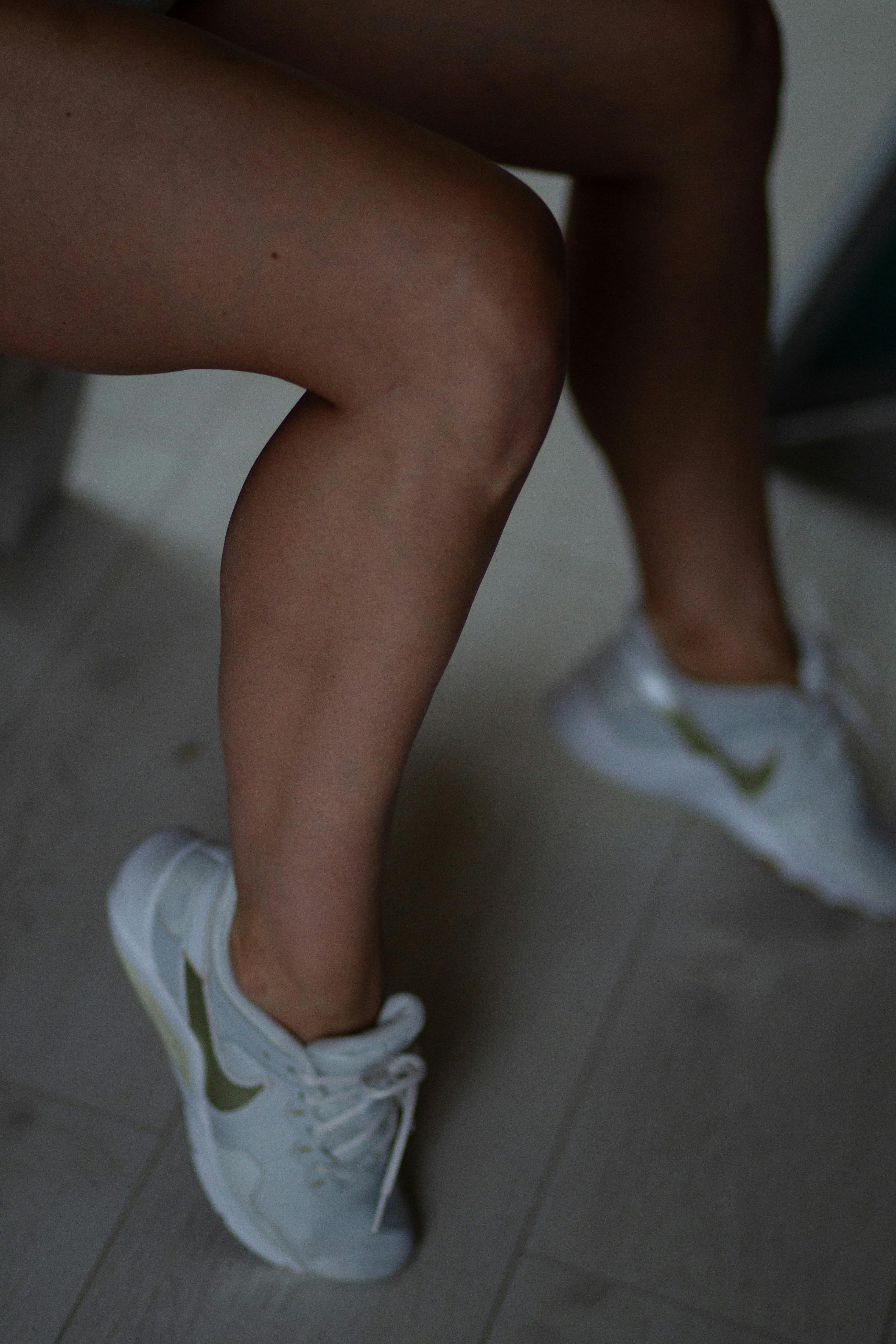 A close shot of a woman's legs in white sneakers against a wooden floor.
