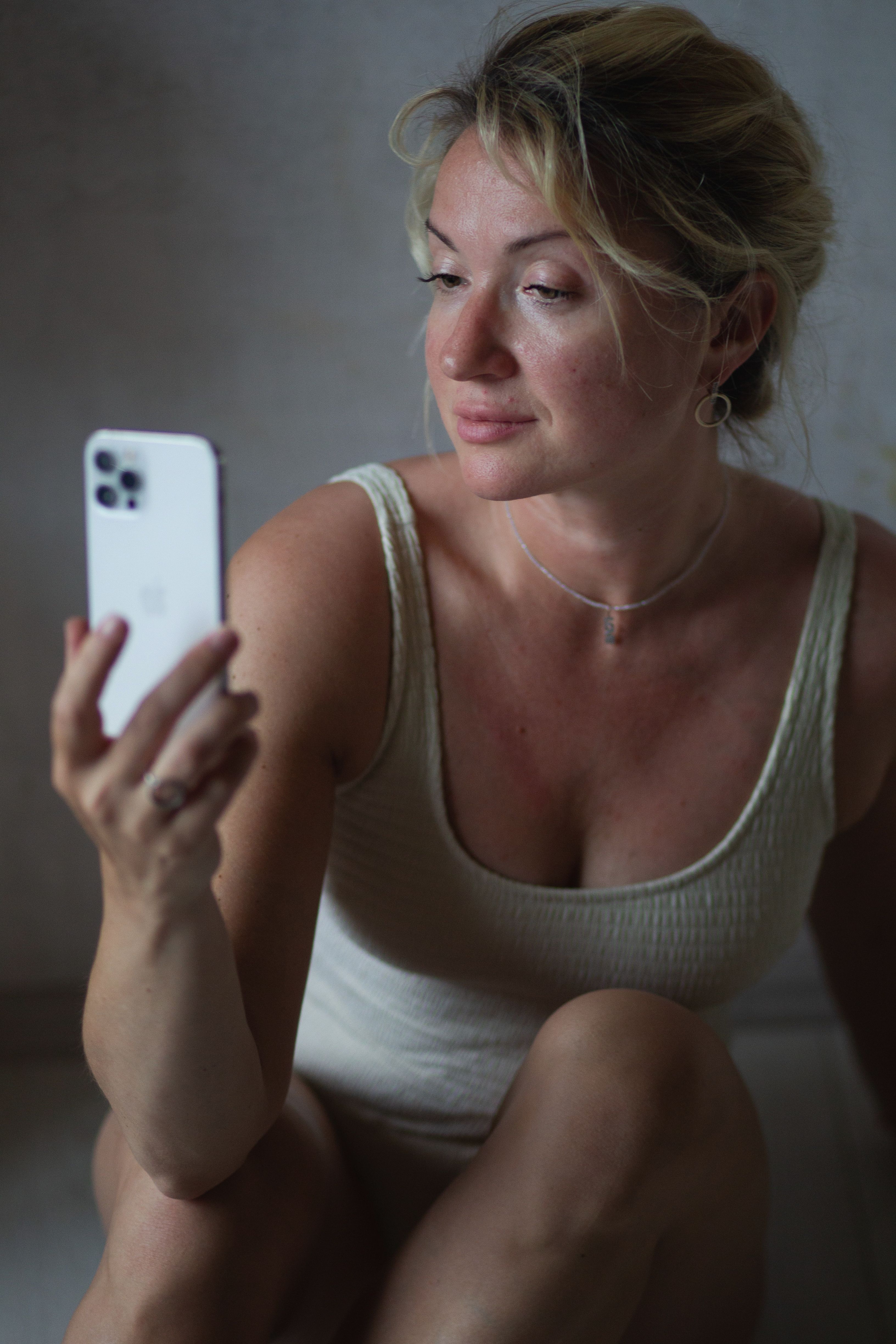 A woman taking a selfie indoors with an iPhone, capturing a casual and relaxed moment.