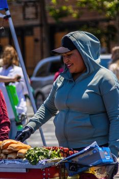 A friendly vendor in a hoodie at a lively street market stand selling fresh produce.