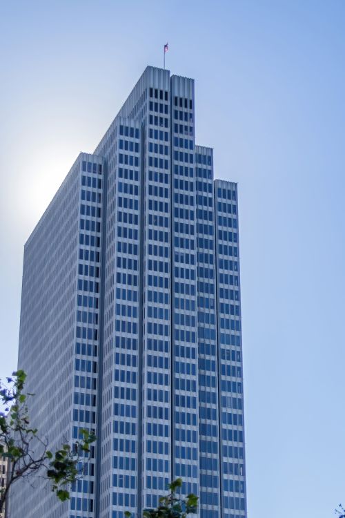 Free A tall modern skyscraper with reflective windows under a clear blue sky. Stock Photo