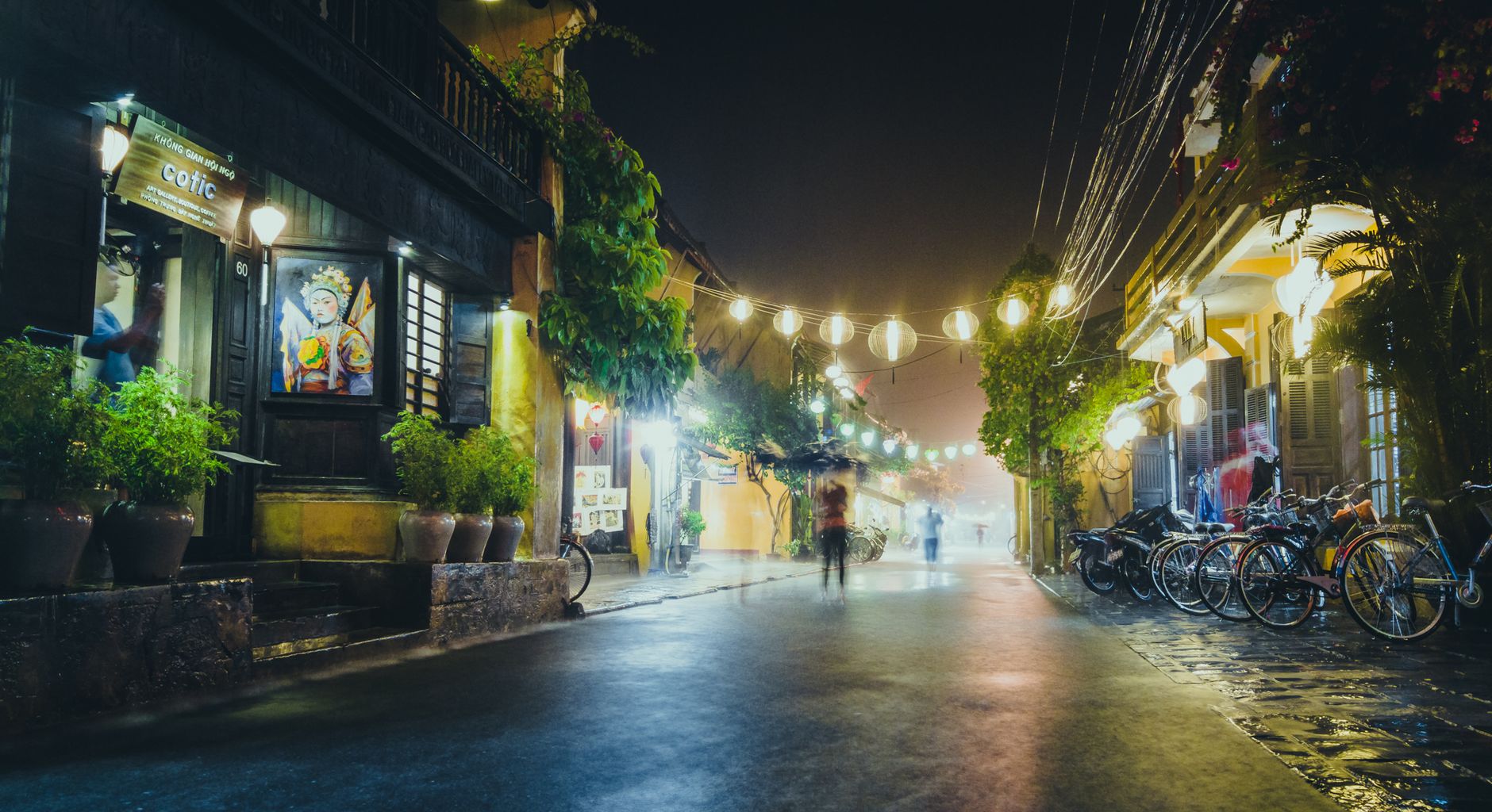 A peaceful street scene at night with hanging lanterns, bicycles, and vibrant lighting.