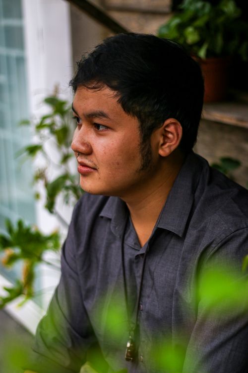 Free Side profile of a young man in thoughtful pose, surrounded by greenery. Stock Photo