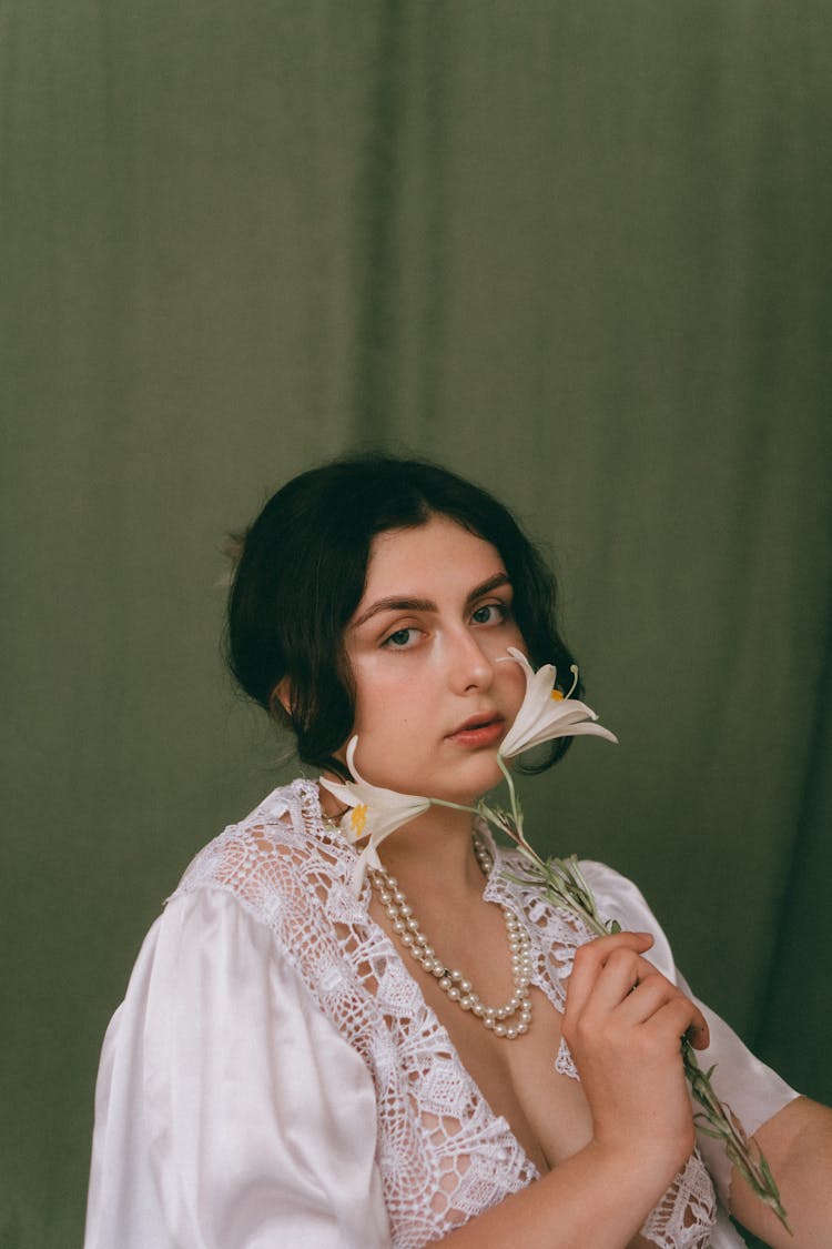 Young Brunette Woman In White Lace Dress Holding A Lily Flower