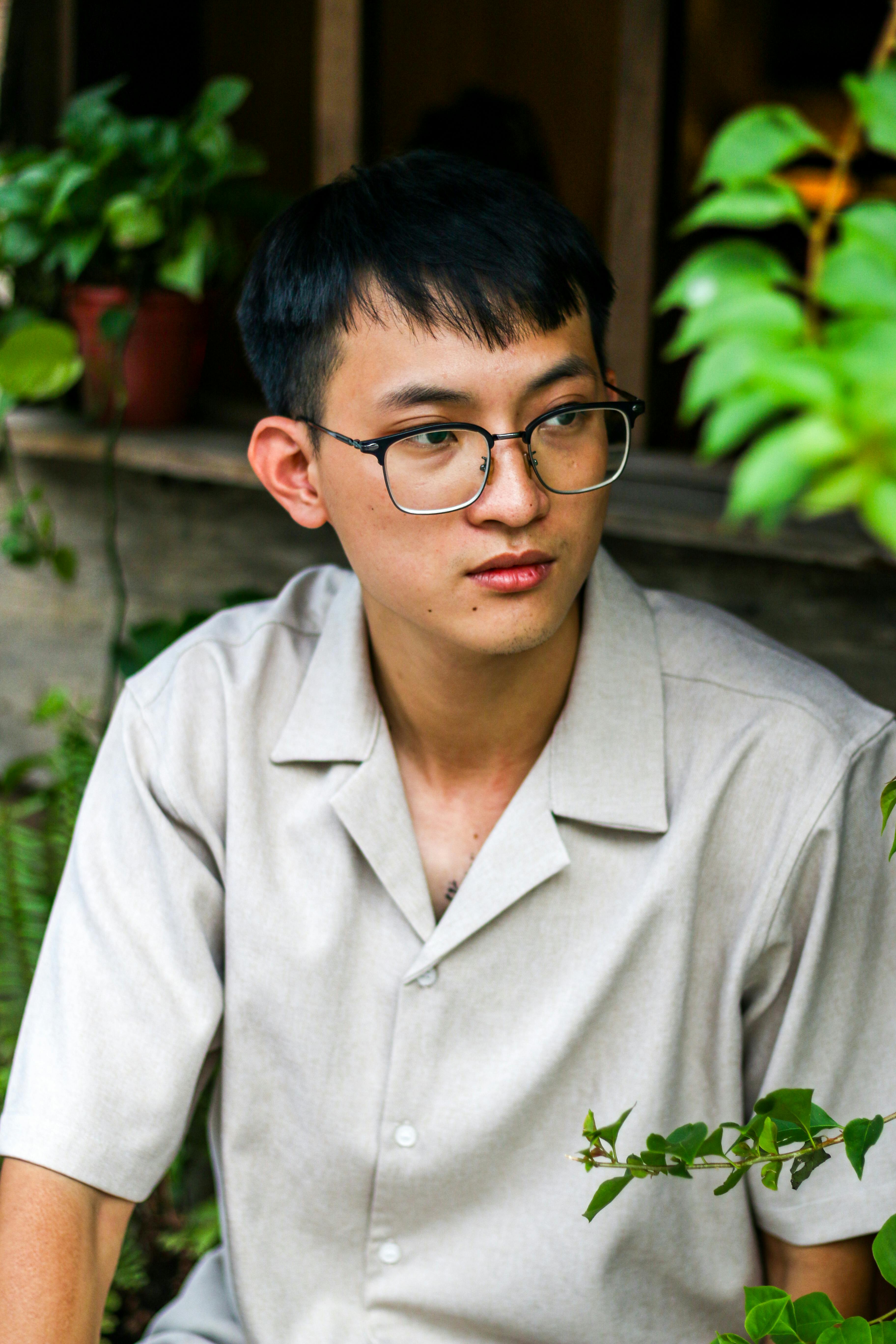 Close-up portrait of an Asian man wearing glasses, with a neutral expression in an outdoor setting.