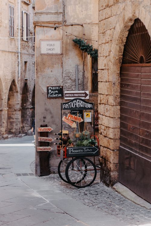 Free A picturesque scene in an old town with a vintage fruit cart and stone buildings. Stock Photo