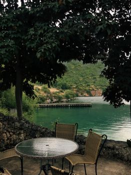 Tranquil lakeside scene with outdoor chairs and lush greenery, perfect for relaxation.