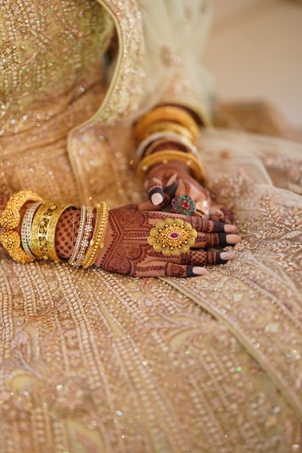 Close-up of a bride's ornamented hand with henna, jewelry, and wedding dress.