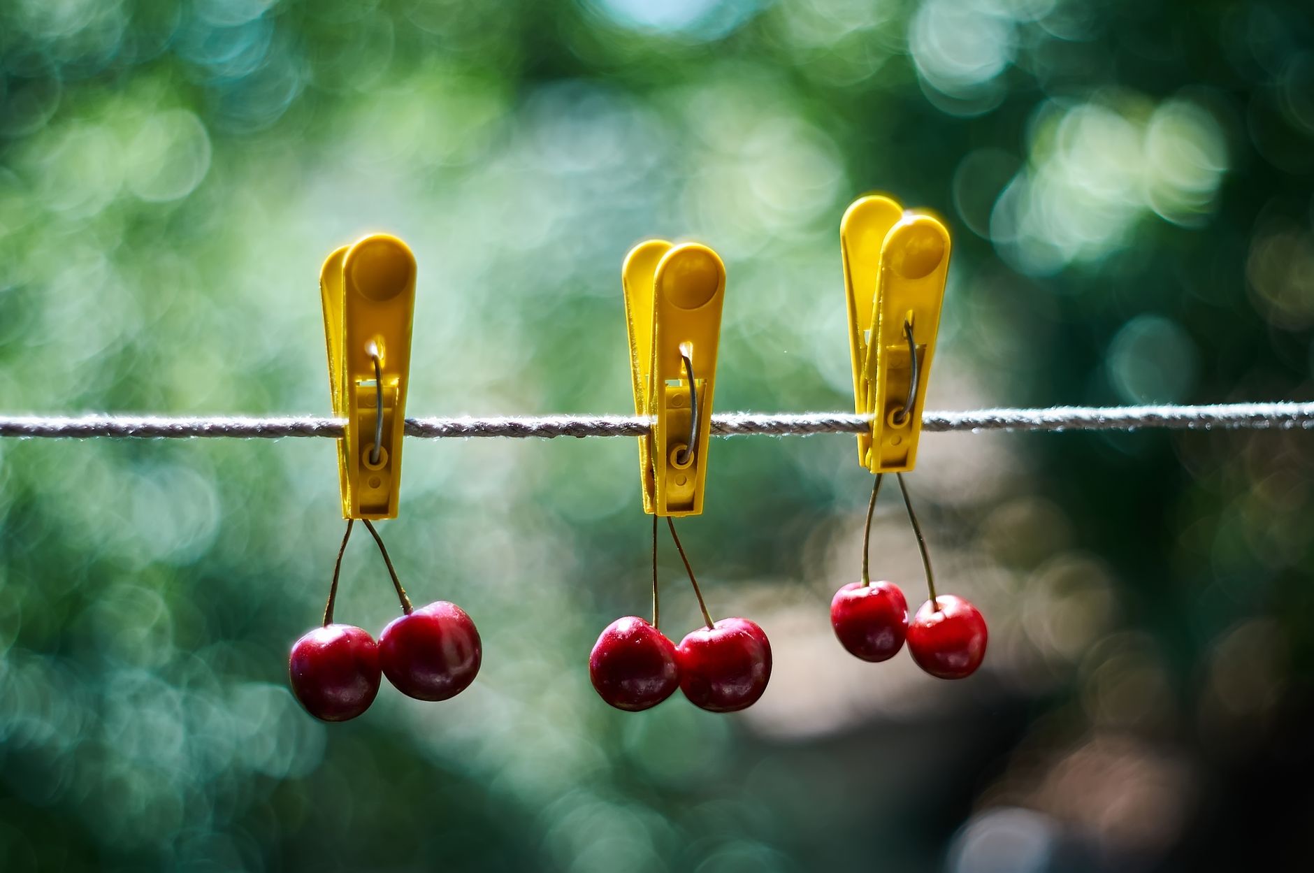 Three cherries on rope with yellow clothespins and green bokeh background.