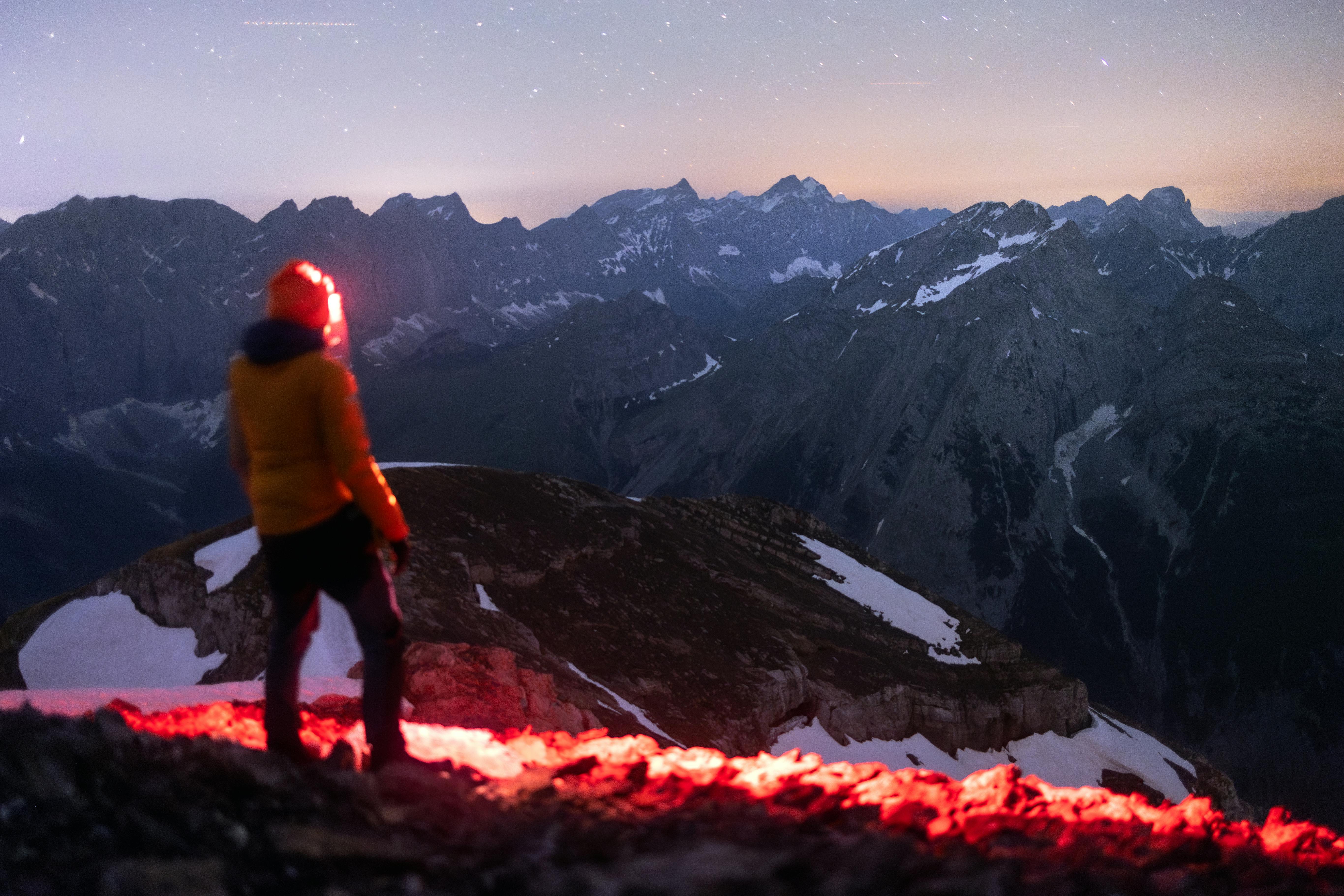 Prescription Goggle Inserts - A lone hiker with a headlamp stands on a mountain peak under a starry Alpine night sky.