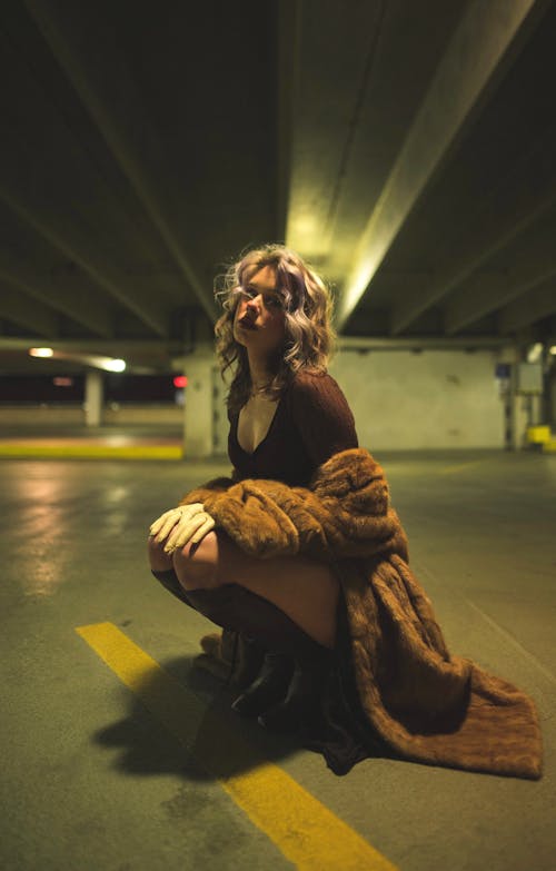 Young Woman in Long Fur Coat Sitting on the Ground in a Parking Garage