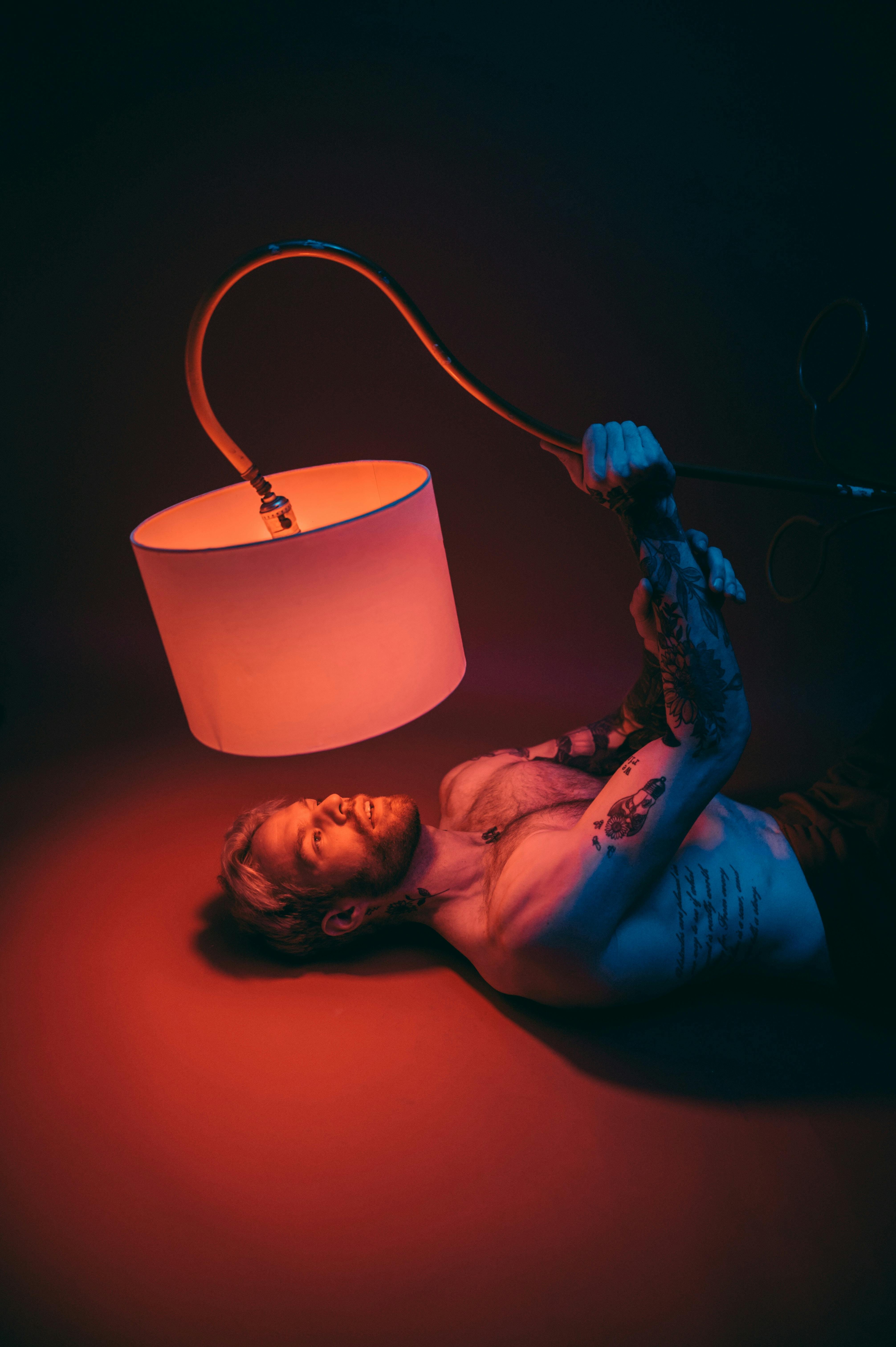 An artistic image of a tattooed male lying under a glowing lamp, creating vibrant lighting effects.
