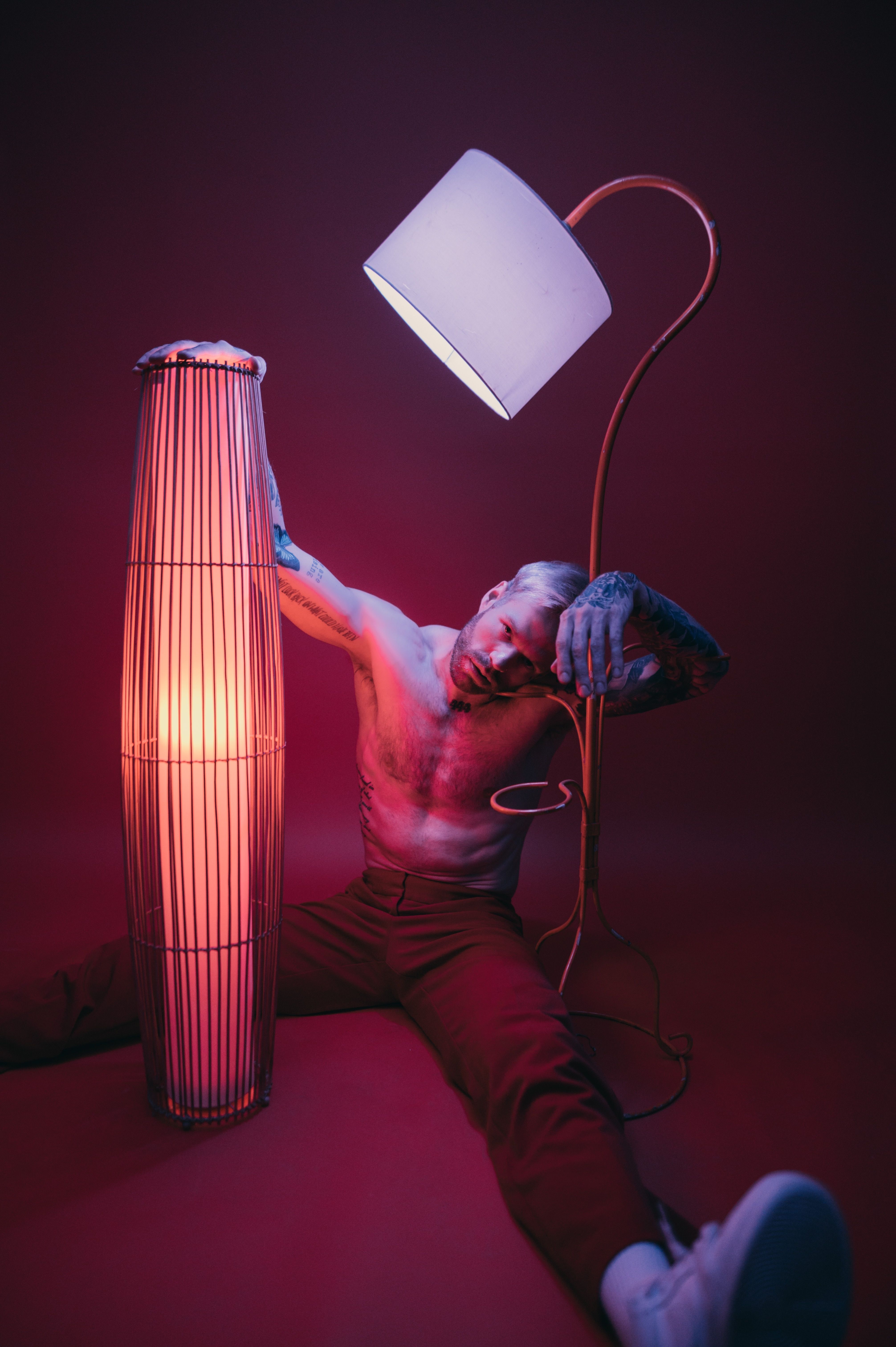 Tattooed man posing with artistic lighting and lamps in a dramatic setting.
