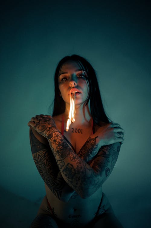 Young Tattooed Woman in Underwear Holding a Burning Torch in Her Teeth