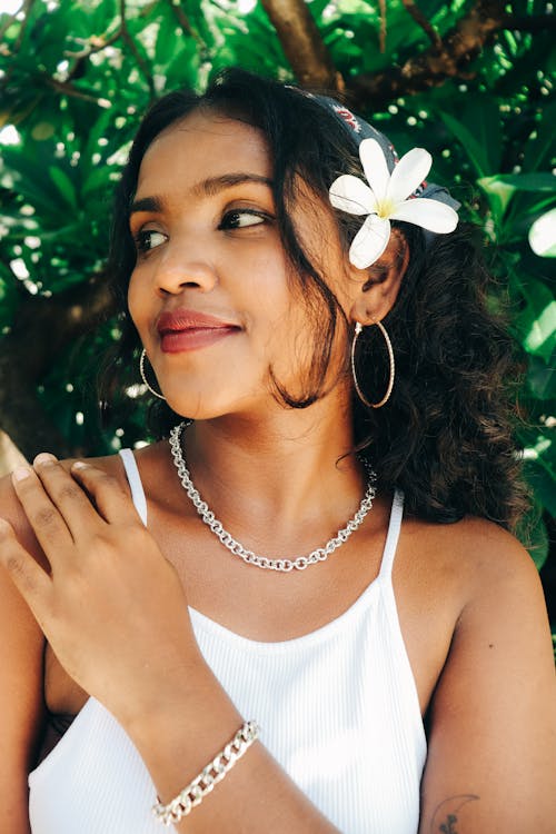 Brunette Woman with a White Flower in Her Hair Posing with a Silver Necklace and Bracelet