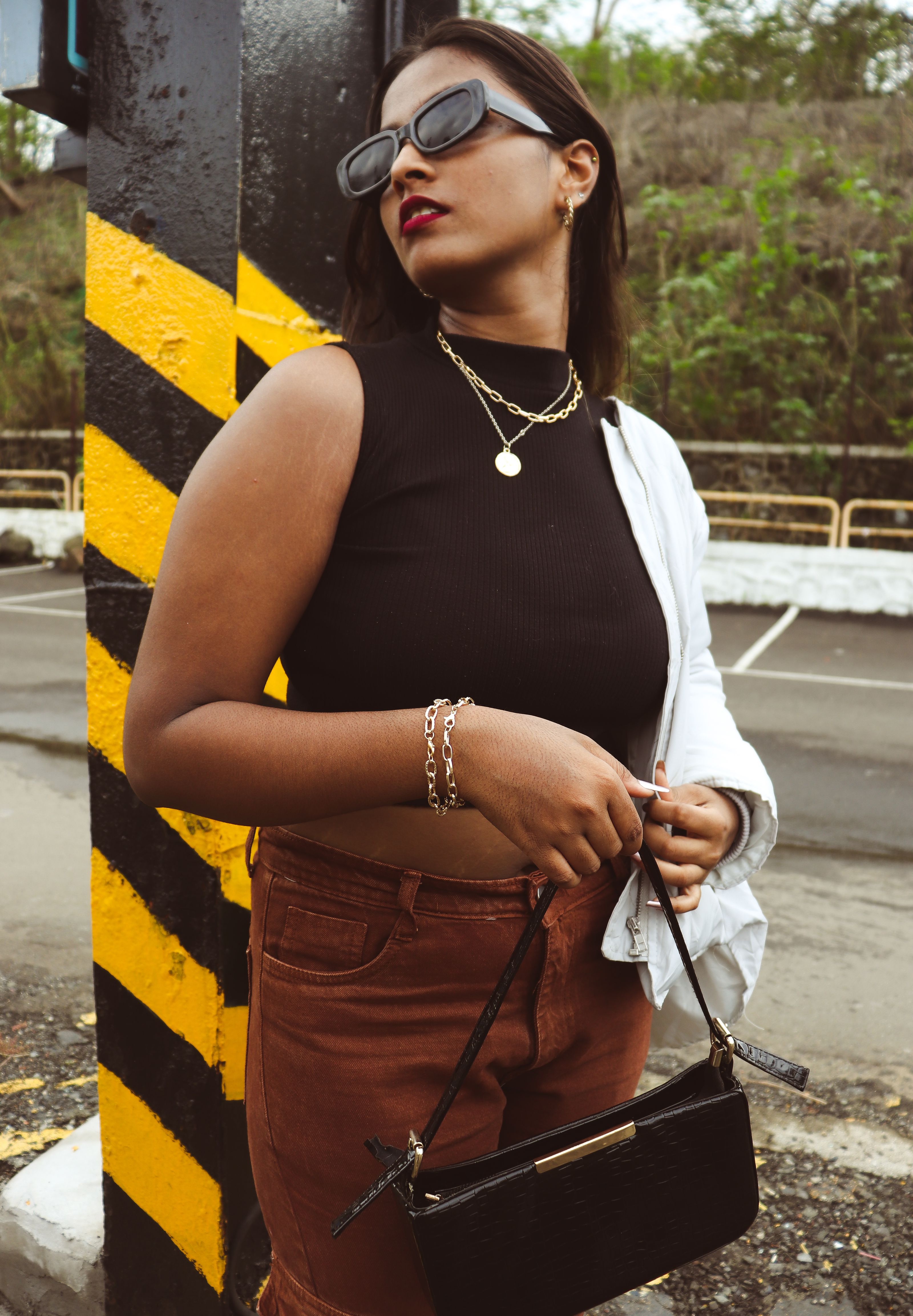 Jovem mulher fashion posando ao ar livre com óculos de sol e bolsa estilosa.