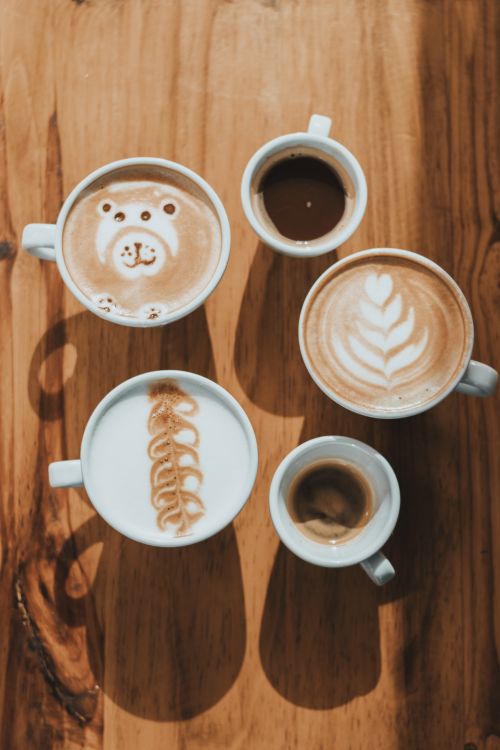 Free Creative coffee art displayed beautifully in a variety of cups on a wooden table. Stock Photo