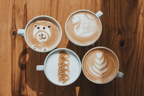 Free Four cups of creative latte art designs on a wooden table, showcasing intricate coffee art. Stock Photo