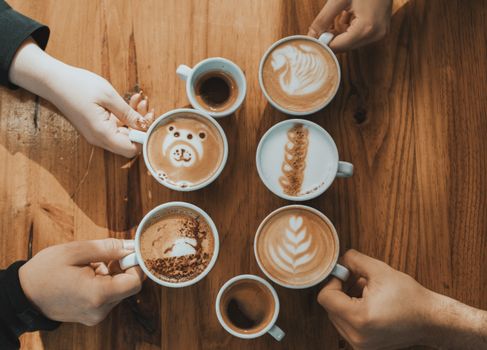 Various artistic lattes arranged on a wooden table, captured from above.