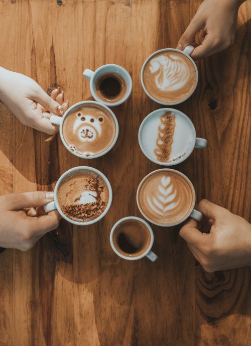 Free Creative latte art designs on multiple coffee cups arranged on a wooden table, captured from above. Stock Photo
