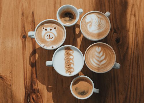 Free Top view of six cups featuring creative latte art designs on a wooden table. Stock Photo