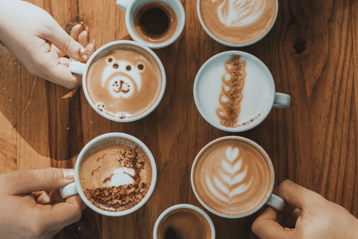 Top view of hands holding coffee cups with latte art on a wooden table