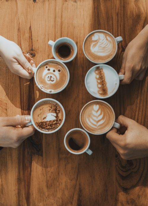 Free A creative display of latte art in a cafe, showing diverse coffee designs held by hands on a wooden table. Stock Photo