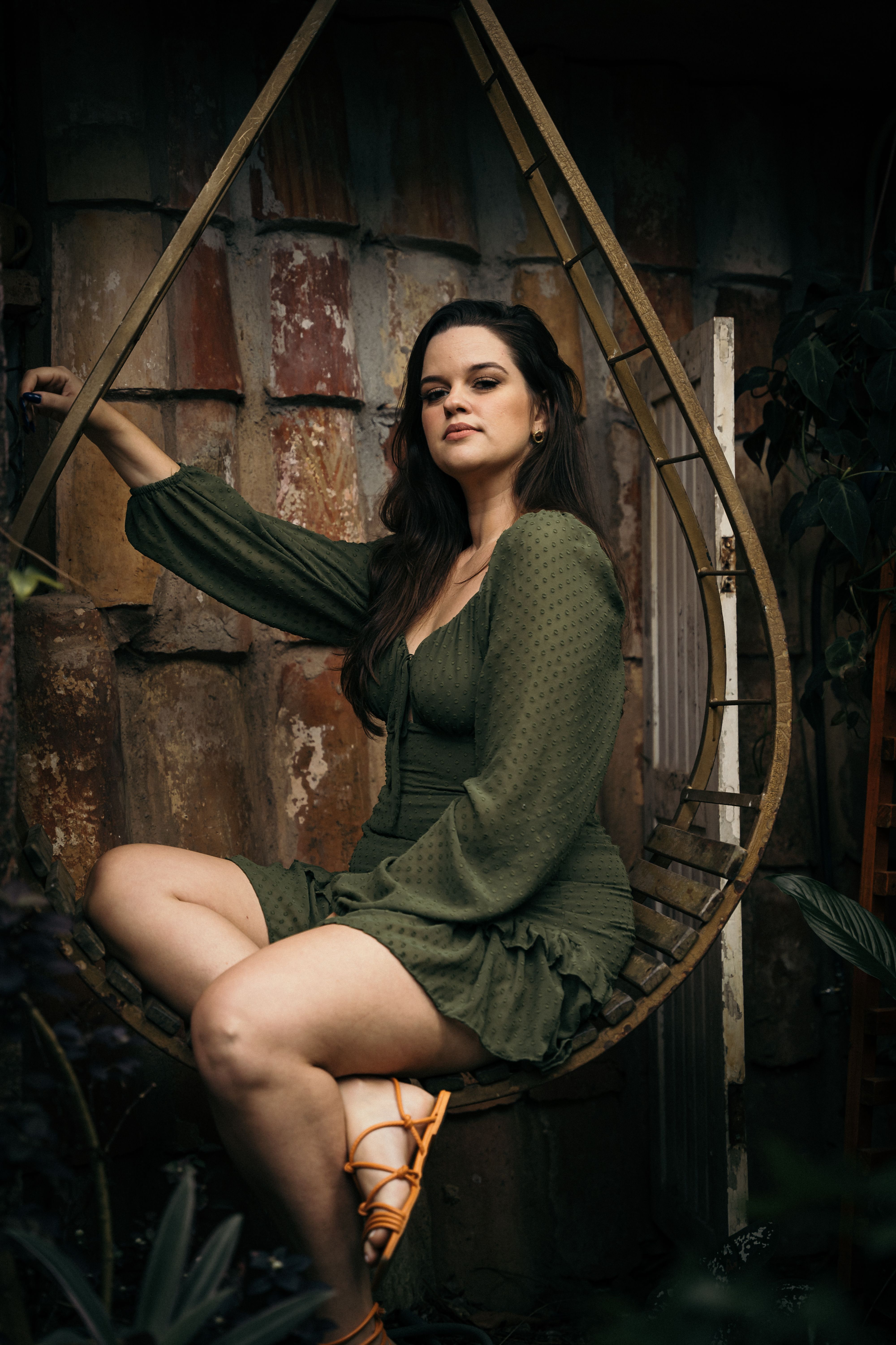 Stylish woman in a green dress sitting on a swing chair outdoors.