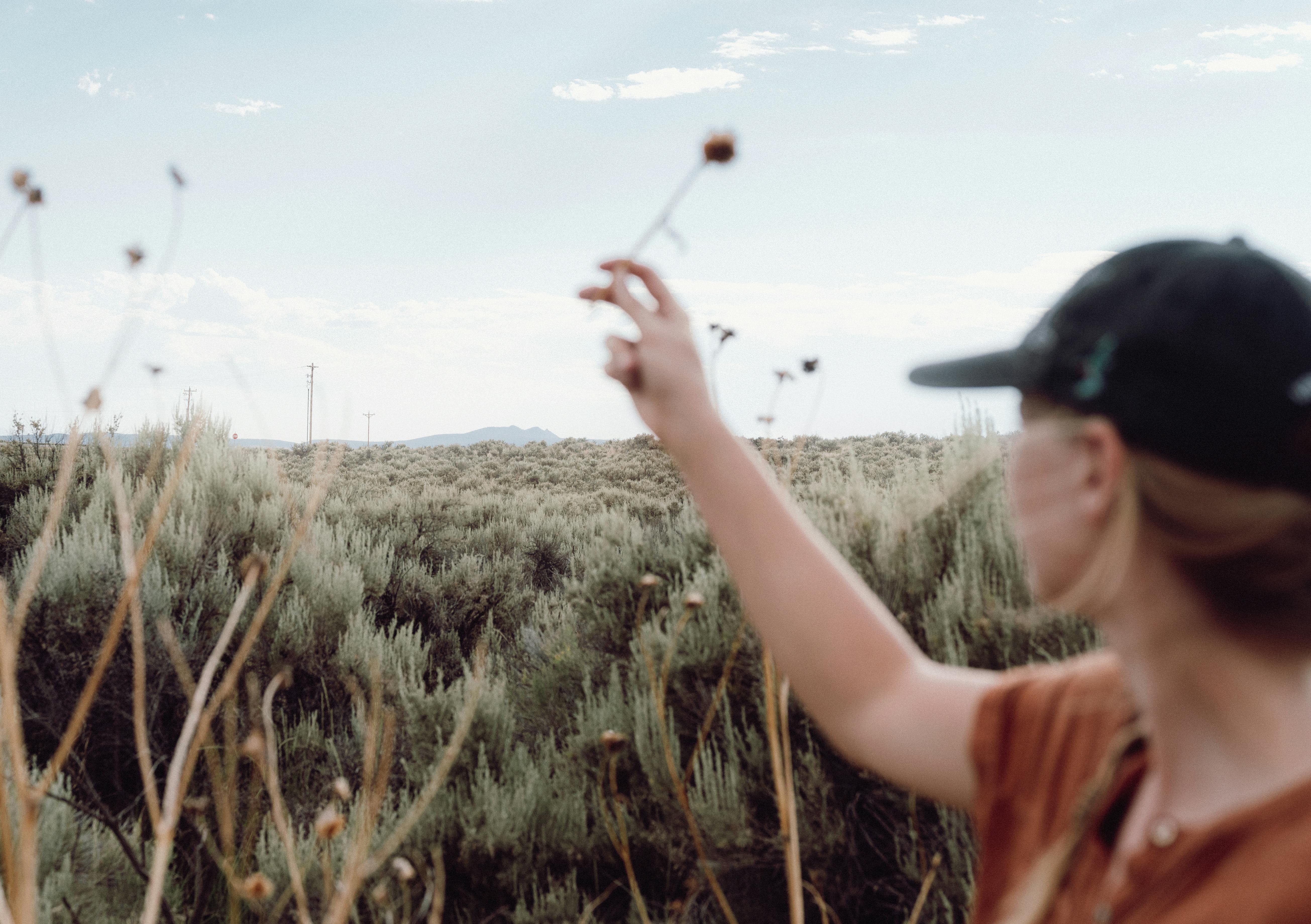 A woman enjoys a serene moment in a vast rural landscape, holding a wildflower.