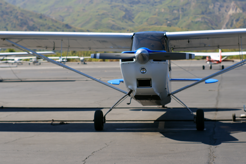 Free Close-up of a small propeller plane parked on a sunny airport tarmac with mountains in the background. Stock Photo