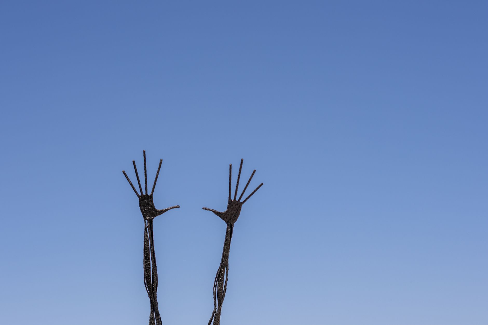 Abstract metal sculpture of hands reaching towards the clear blue sky, highlighting artistic expression.