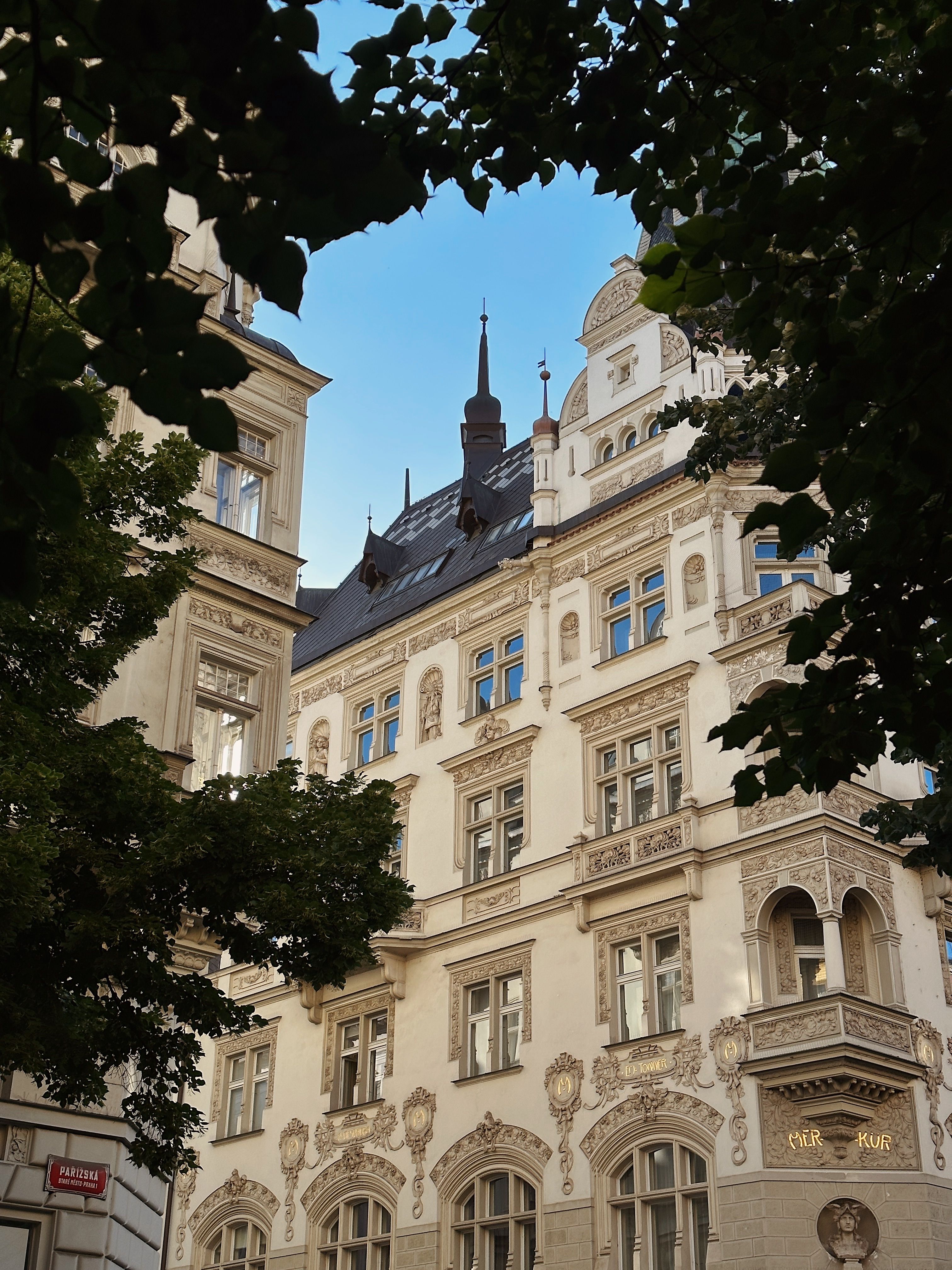 Elegant neoclassical building facade framed by lush trees in Prague, Czechia.