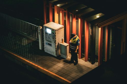 Free A security guard checks his smartphone beside an illuminated vending machine at night. Stock Photo