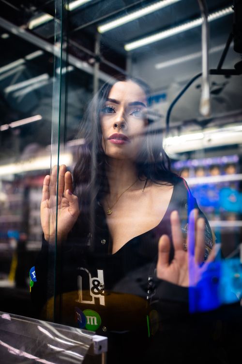Free A brunette woman gazes through a glass pane, creating a reflective portrait in a store setting. Stock Photo