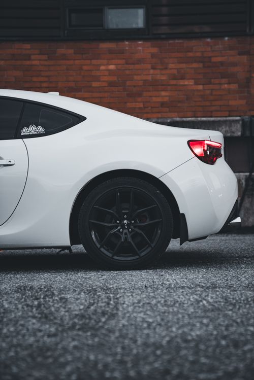 Free Side view of a white sports car parked on a city street, showcasing sleek design and alloy wheels. Stock Photo