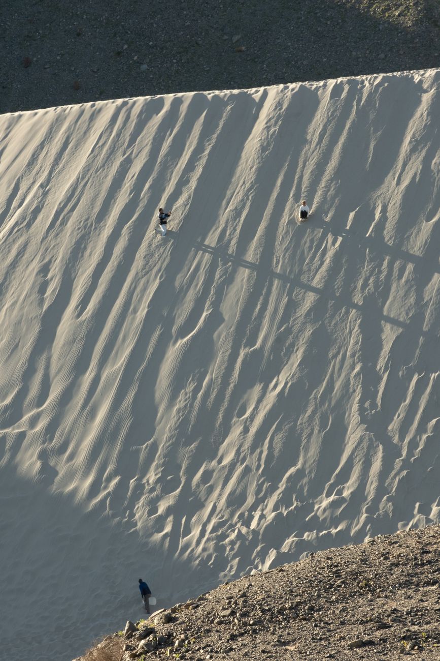 Three people ascend a steep desert sand dune under soft twilight lighting, casting long shadows.. pexels, three, people