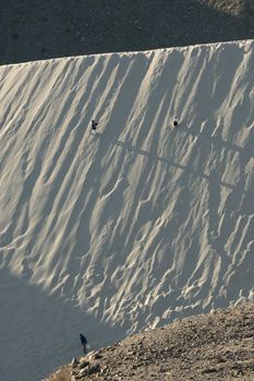 Three people ascend a steep desert sand dune under soft twilight lighting, casting long shadows.. pexels, three, people