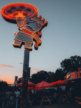 Vibrant neon pizza sign illuminating a pizzeria at sunset, creating a nostalgic ambiance outdoors.