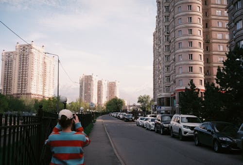Woman Taking a Picture of a Street and Modern Apartment Buildings in City 