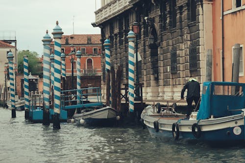 View of a Man Standing on a Boat near a Dock on the Canal in Venice, Italy 