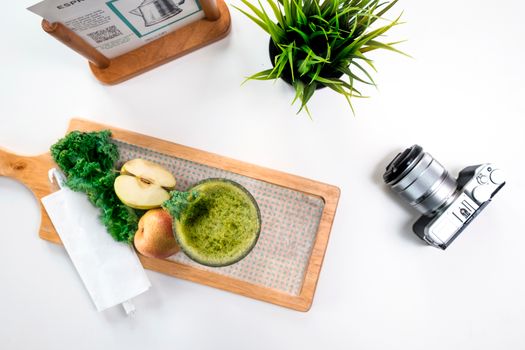 Top view of a green detox smoothie with fresh apples, kale, and a camera on a wooden board.